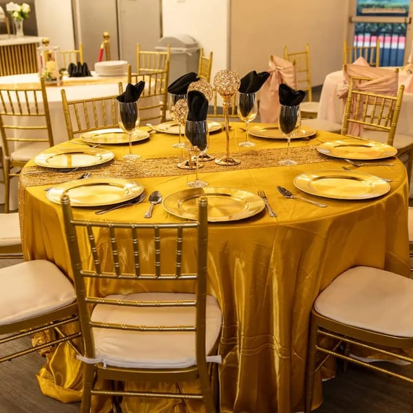 A round table set with golden plates, black napkins, and gold chairs in a banquet hall.