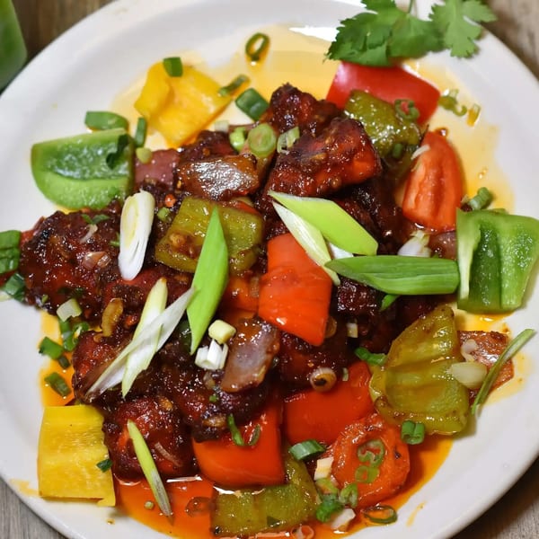 Sweet and sour chicken with bell peppers and green onions on a white plate.