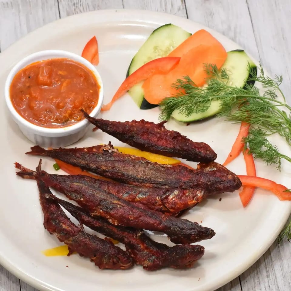 Fried fish with a side of red sauce, sliced cucumbers, carrots, and dill on a white plate.
