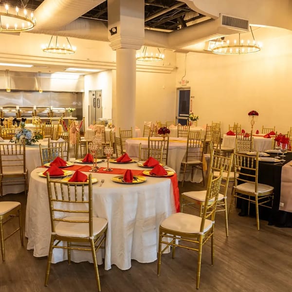 Elegant banquet hall with round tables, gold chairs, red and black tablecloths, and buffet stations.