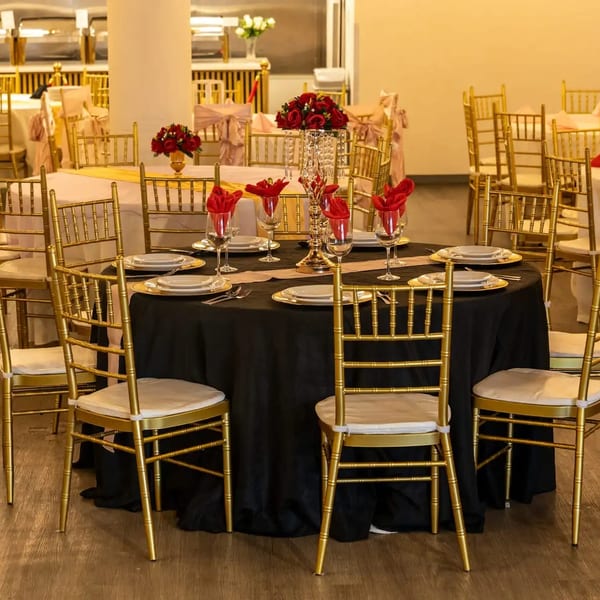 Elegant dining room with round tables, gold chairs, black and white tablecloths, and red floral centerpieces.