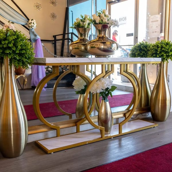 Elegant gold and marble console table with floral arrangements, reflecting in a large mirror.