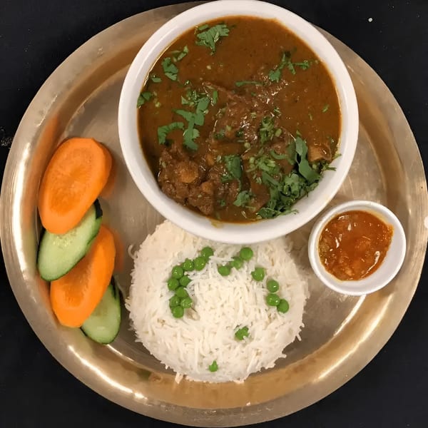 A Nepali thali with chicken curry, rice with peas, sliced carrots, cucumbers, and chutney.