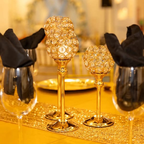 Elegant table setting with golden accents, crystal candle holders, and black napkins in wine glasses.