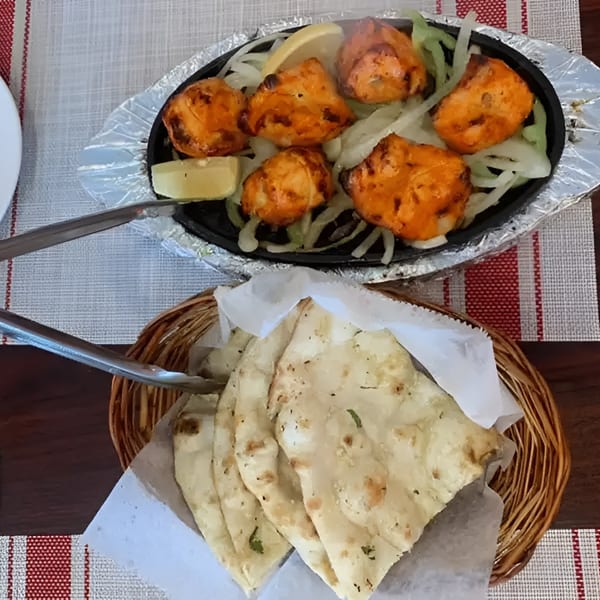 Sizzling chicken tikka with onions and lemon, alongside a basket of naan bread on a table.